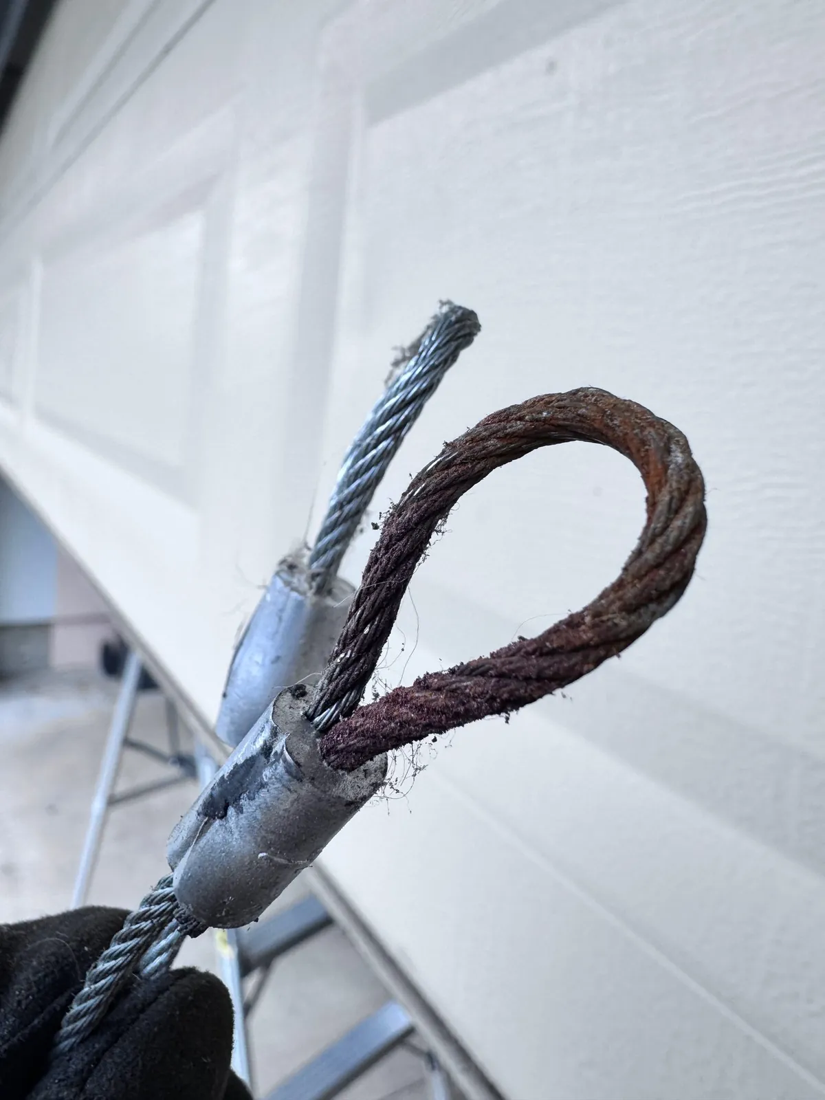 Snapped, rusted garage door lift cable held up beside the door — a common emergency failure